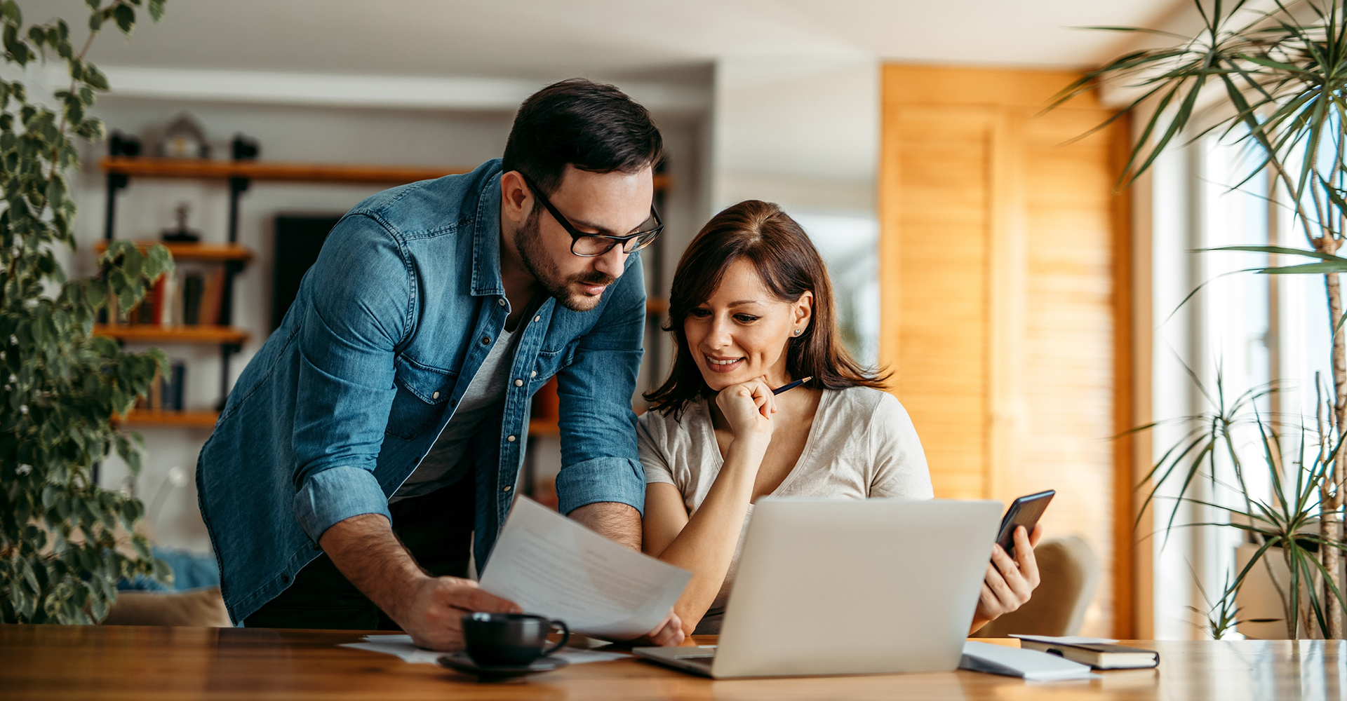 Middle age couple looking at finances on a computer screen, mobile device, and on paper